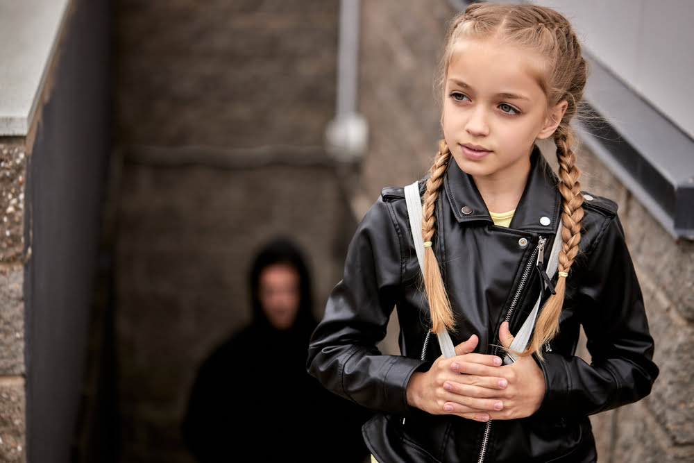 a man in a hoodie sneaks up on a young girl to illustrate the crime of soliciting a minor for sex