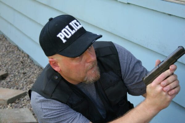 An officer squats with gun drawn. New AI technology could allow him to write a police report based on statements he makes into his bodycam.